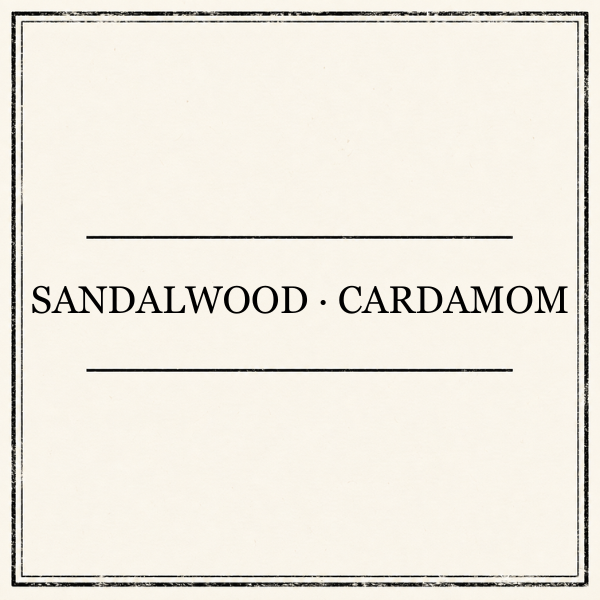A square kraft-paper style label or packaging card with the words “SANDALWOOD • CARDAMOM” printed in black serif text between two horizontal lines.